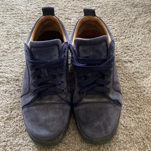 Slitna Louboutins (marinblåa) - Säljer ett par snygga blå sneakers i mocka med klassisk röd sula och mörkblå snörning. Skorna har rund tå och platt sula, samt beige insida. Perfekta för dig som vill ha en stilren och unik look.