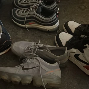 Nike sneakers i olika modeller - 4 par Nike sneakers: ett par Nike Air Max 97 i svart, grått och vitt med reflekterande detaljer, ett par Nike Vapormax i ljusgrått med svart swoosh och transparent sula, samt ett par svartvita Nike Jordan med svarta och röda och gröna detaljer och Jordan 4 starfish kolla de individuella inläggen för pris osv 