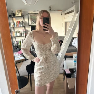 Blommig kortklänning från Adoore - Supersöt kortklänning från Adoore i storlek 34. Klänningen är ljus med små gula blommor, har långärmade puffärmar, v-ringning och snörning framtill. Perfekt för vår och sommar, och ger en romantisk vibe. Säljer vidare då den var lite för stor. 