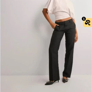 Lågmidjade Svarta kostymbyxor  - Snygga svarta kostymbyxor med klassisk rak passform och pressveck. Byxorna är lågmidjade hällor för bälte och stängs med dragkedja och knapp. Perfekta för en stilren look.