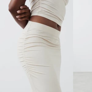 Beige långklänning med rynkdetaljer - Elegant beige långklänning med rynkdetaljer som ger en smickrande passform. Klänningen har en hög hals och är ärmlös, vilket ger en stilren look. Perfekt för en chic och modern stil. Säljer  för original pris då den aldrgi är använd  stl s 