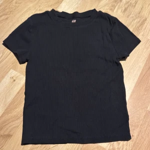 Svart ribbad t-shirt från H&M - Säljer en svart ribbad t-shirt från H&M i ekologisk bomull. Den har en enkel design med korta ärmar och rund hals. Perfekt för en avslappnad stil. 🖤