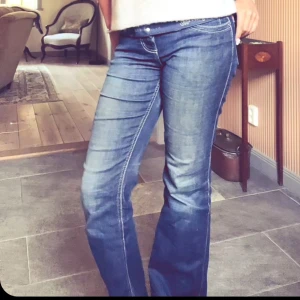 Blå jeans från Wrangler - Snygga blå jeans från Wrangler med bootcut-stil. De har dekorativa detaljer på bakfickorna och en klassisk femficksdesign. Perfekta för en avslappnad look. Dem har hål/slitningar vid innerlåren därav priset 