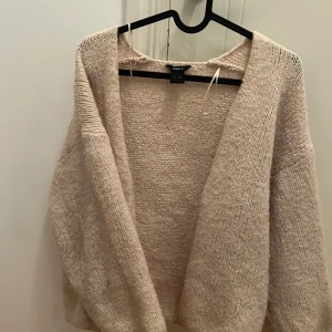 Beige stickad kofta från Lindex - Mysig beige stickad kofta från Lindex i storlek XS. Koftan har en öppen design utan knappar och långa ärmar.