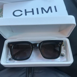 Svarta solglasögon från CHIMI - Snygga svarta solglasögon från CHIMI med en stilren och fyrkantig design. De kommer i ett elegant vitt fodral med en skyddande påse. Perfekta för att ge en cool touch till din stil. Perfekt till vår och sommar, passar till damer och herrar 