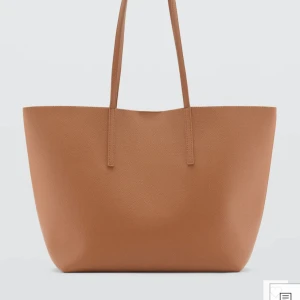 Beige shoppingväska - Snygg och rymlig beige shoppingväska. Perfekt för att bära med sig allt man behöver under dagen. Väskan har en stilren design med två långa handtag för enkel bärning.