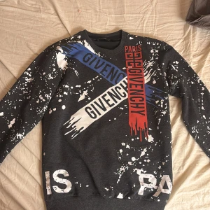 Grå sweatshirt från Givenchy - Säljer en grå sweatshirt från Givenchy med färgstarka tryck i rött, blått och vitt. Tröjan har ett unikt stänkmönster och långa ärmar. Tror inte den är äkta, säljer denna för det är mitt ex och han har inte häntat den. Pris går att förhandla vill bara bli av med den