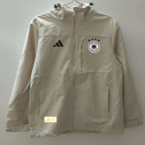 Beige vindjacka från Adidas - Säljer en beige vindjacka från Adidas med Tysklands landslagsmärke på bröstet. Jackan har en huva och dragkedja framtill samt två sidofickor. Perfekt för blåsiga dagar!