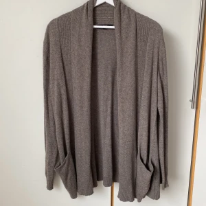 Mysig brunmelerad kofta från Lindex - En mysig brunmelerad kofta från Lindex. Den har ribbad sjalkrage, långa ärmar och fickor. Lös modell utan knäppning vilket gör den lätt att slänga på sig över en topp eller blus. Längd 80 cm. 