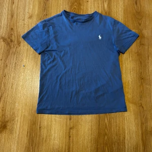 Blå t-shirt från Ralph Lauren - Säljer en klassisk blå t-shirt från Ralph Lauren med korta ärmar och det ikoniska logotypbroderiet på bröstet. Perfekt för en avslappnad stil. Skön och enkel att matcha med det mesta. 💙