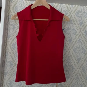 Röd ärmlös topp med krage - Tajt trikå topp med krage, tidigare varit ett snöre till som inte längre finns kvar, använt utan snöre. Står ej storlek men skulle säga S 