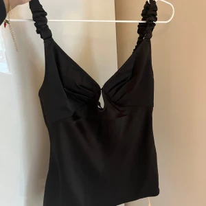 Svart topp från ADOORE - Snygg svart topp från ADOORE med rynkade axelband och en liten öppning framtill. Oanvänd