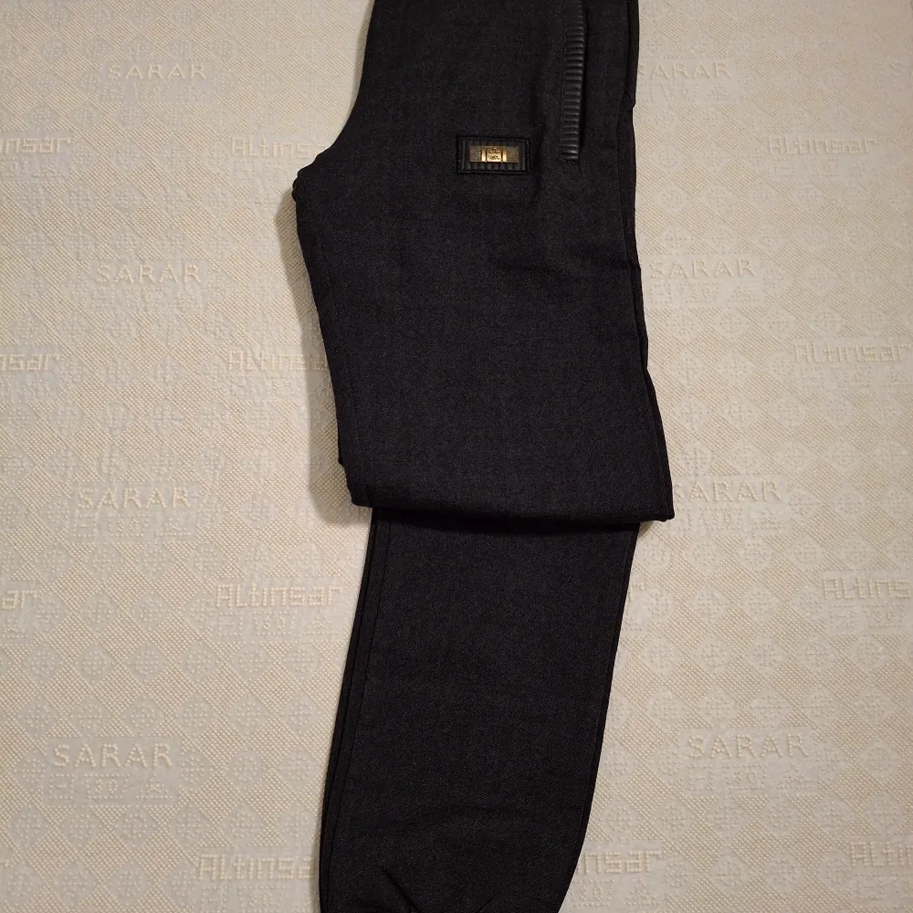 Snygga mörkgrå byxor med dragkedjor vid fickorna och en diskret logga på sidan. Byxorna har en modern och stilren design, perfekt för en avslappnad look. De är tillverkade i ett bekvämt material som ger en skön passform.. Farkut & Housut.
