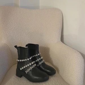 Svarta boots med pärldetaljer - Snygga svarta boots med dekorativa pärlor runt skaftet och foten. De har en robust sula. Perfekt för dig som vill sticka ut! Storlek 36 