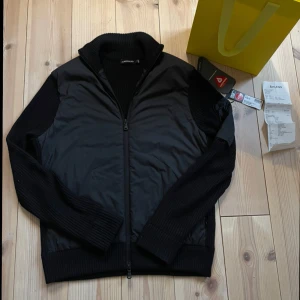 J.Lindeberg Cardigan - En riktigt stilren cardigan från J.Lindeberg. Den är i prima skick, använd fåtal gånger. Storlek S och den är svart. Tag, kvitto och påse finns. Nypris:3200kr Mitt pris:1499