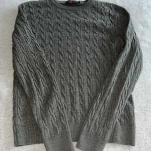 Grön kabelstickad tröja från Morris - Säljer en stilren olivgrön kabelstickad tröja från Morris i 100% merinoull. Tröjan har en broderad detalj på bröstet och långa ärmar. Perfekt för kyligare dagar.Nypris ca 1800kr mitt pris 449kr. Pris inte hugget i sten🙌