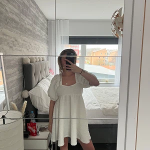 Vit kortklänning med puffärmar - Söt vit kortklänning med puffiga kortärmar och en luftig passform. Perfekt för sommarens alla fester och studentfiranden. Klänningen har en enkel och stilren design som gör den lätt att matcha med olika accessoarer. 