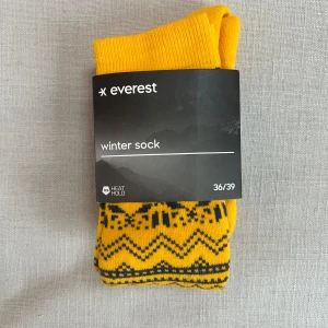 Gula vinterstrumpor från Everest - Säljer ett par gula vinterstrumpor med mörkblått mönster ifrån Everest. Strumporna är designade för att hålla värmen med Heat Hold-teknologi och har elastiskt stöd för fotvalv och anklar. Strumporna är i nyskick och är helt oanvända. Nypris 130, säljer för 50! strl 36-39💗