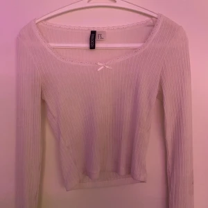 Vit topp med spets från Newyorker  - Säljer en söt vit ribbad topp från newyorker. Toppen har långa ärmar och en liten rosett framtill. Den är dekorerad med spetsdetaljer vid halsringningen. Perfekt för en stilren look. Finns dock några små fläckar på men jag tror att de flesta skulle gå bort i tvätten.