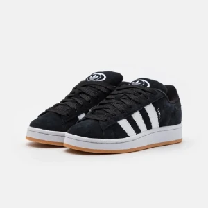 Svarta sneakers från Adidas - Snygga svarta sneakers från Adidas med klassiska vita ränder på sidan. Skorna har en gummisula i ljusbrun färg och snörning framtill. Perfekta för en stilren look.