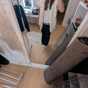 Vit pälsväst med huva - Säljer en fluffig vit pälsväst med huva. Västen är perfekt för att hålla sig varm och stilren under kyligare dagar. Den har en mjuk insida och en elegant look.