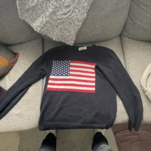 Svart tröja med amerikansk flagga - Säljer en svart tröja med en stor amerikansk flagga på framsidan. Tröjan har långa ärmar och en avslappnad passform. Perfekt för en casual look.