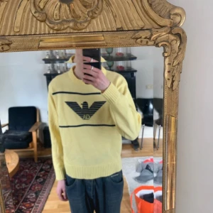 Gul tröja från Emporio Armani - Säljer en gul tröja från Emporio Armani med svart logotyp och ränder. Tröjan har långa ärmar och ribbade muddar vid ärmslut och nederkant.