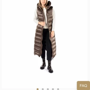 Brun lång dunväst med huva - Snygg och lång brun dunväst med dragkedja och huva. Perfekt för kyliga dagar när du vill hålla dig varm och stilren. Västen har en quiltad design som ger en modern look.