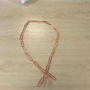 Halsband av kopparfärgade gem - Unikt halsband tillverkat av kopparfärgade gem. Designen är enkel men iögonfallande, perfekt för den som vill ha något annorlunda. Gemmen är sammanlänkade för att skapa en kedja med en kreativ touch.