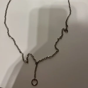 Silverfärgat halsband med ringdetalj - Elegant silverfärgat halsband med en enkel kedja och en ringdetalj som hänger ned. Perfekt för att ge en stilren touch till din outfit.
