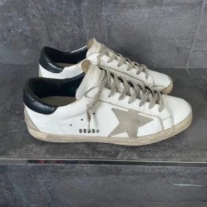 Vita sneakers med stjärndetalj - Snygga vita sneakers med en grå stjärna på sidan och svarta detaljer vid hälen. Skorna har snörning och en stilren design som passar perfekt till vardags. De har en bekväm passform och är tillverkade i skinn.