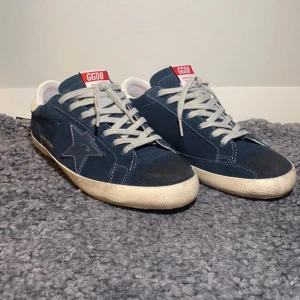 Blå sneakers från Golden Goose - Snygga blå sneakers från Golden Goose med en stjärndetalj på sidan. Skorna har grå snörning och en vit sula med en lätt sliten look. Perfekta för en avslappnad stil.