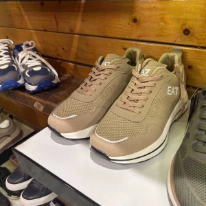 Beige sneakers från EA7 - Snygga beige sneakers från EA7 med vit sula och diskret logga på sidan. Skorna har snörning och en stilren design som passar perfekt för en avslappnad look. MÅNGA STORLEKAR FINNS 