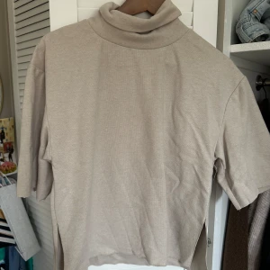 Beige polotröja från Zara - Säljer en stilren beige polotröja från Zara. Tröjan har en klassisk polokrage och korta ärmar, perfekt för lager-på-lager eller som den är. Materialet känns mjukt och bekvämt mot huden.