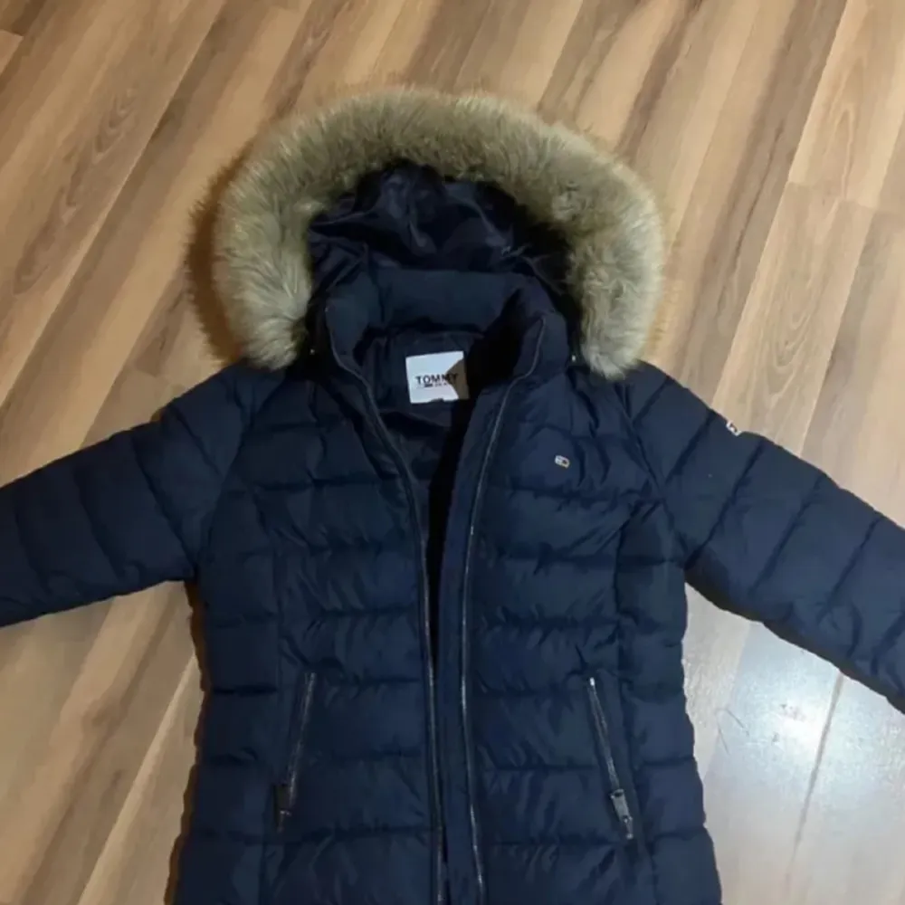 Snygg mörkblå dunjacka från Tommy Hilfiger med pälskantad huva. Jackan har dragkedja och knappar framtill samt två fickor med dragkedja. Perfekt för kalla dagar!. Takit.