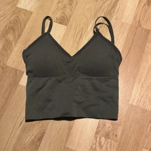 Mörkgrön ribbad linnetopp - Säljer en snygg mörkgrön ribbad sporttopp med smala axelband och v-ringning. Perfekt för en stilren look. Aldrig använd