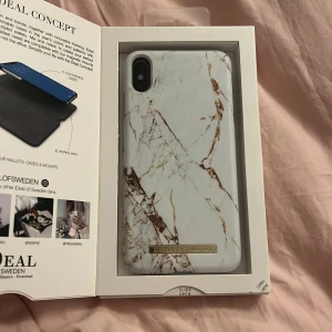 Carrara Gold mobilskal från iDeal of Sweden - Snyggt mobilskal i marmorlook med guldiga detaljer från iDeal of Sweden. Passar iPhone XS Max. Skalet har en elegant design med en vit bas och gyllene marmoreringar, vilket ger en lyxig känsla. Perfekt för att skydda din telefon med stil.