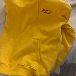 XQS mearch  - Säljer en gul hoodie från XQS med texten 'CHILI MANGO' broderad på bröstet. Tröjan har en klassisk design med känguruficka och ribbade muddar vid ärmslut och nederkant. Perfekt för en färgglad stil! Passar alla som har S-L ( har själv L)