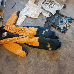 Orange och marinblå overall med stjärnor - Säljer en cool orange och marinblå overall med stjärnmönster. Overallen har dragkedja framtill och reflexdetaljer på benen. Perfekt för lek utomhus! Ingår lite andra barnkläder med 