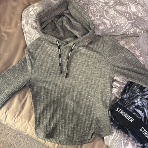 Grå ribbad hoodie från Stronger - Säljer en snygg grå ribbad hoodie från Stronger. Den har en bekväm passform med långa ärmar och en justerbar huva med svarta snören. Perfekt för kyliga dagar eller mysiga hemmakvällar. Aldrig använt. Storlek M men passar en S