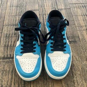 Nike Air Jordans i blått och vitt - Snygga Nike Air Jordans UNC Low i en fräsch blå och vit färgkombination. Skorna har svarta snören och en klassisk Nike-logga på sidan. Perfekta för dig som vill ha en stilren och sportig look. Ny pris - 3499 - Merchsweden.se
