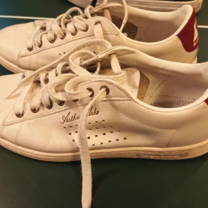 Vita sneakers från Le Coq Sportif och Adidas - Säljer ett par vita sneakers från Le Coq Sportif med röd detalj på hälen och ett par. Perfekta för en sportig look. Båda paren har snörning och är i skinn.
