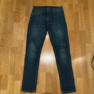 Nudie Jeans - Säljer ett par snygga blå jeans från Nudie i väldigt bra skick. Jeansen har en lätt slitning för en cool look och är perfekta för vardagsbruk. Dom har en väldigt modern och populär slimmad passform. 