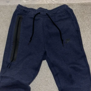 Mörkblå nike tech byxor (helt nya) - (använd 1 gång) Säljer ett par mörkblå mjukisbyxor från Nike med snörning i midjan och en praktisk dragkedja på sidan. Perfekta för en avslappnad stil. Anledningen till att jag säljer varan är för att den var ganska liten på mig och retur funka inte!