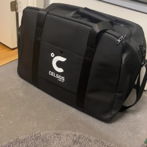 Svart väska från Celsius - Säljer en riktigt skön svart duffelbag från Celsius. Justerbar axelrem samt handtag för att bära. Flera praktiska dragkedjor och fack. Materialet är ett sorts regntätt riktigt snyggt och skönt material. 