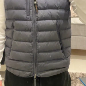 Svart dunväst från Parajumpers - Säljer en svart dunväst från Parajumpers. Västen är superlätt och har en dragkedja framtill samt två fickor med dragkedja. Perfekt för kyligare dagar när du vill hålla värmen utan att känna dig tung. Västen är i bra skick och den är i storlek S