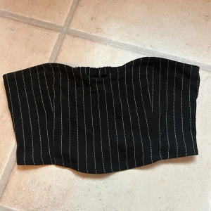 Svart randig tubtopp från Monki - Säljer en svart tubtopp från Monki med vita ränder. Toppen har en elastisk del baktill för bättre pasform.