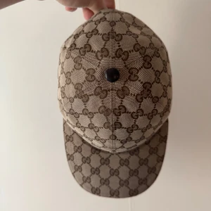 Gucci Keps Beige - Snygg beige keps från Gucci med det ikoniska monogrammönstret i brunt. Kepsen har en justerbar rem baktill och en klassisk skärm. Perfekt för att ge din outfit en lyxig touch.     BYTES GÅR OCKSÅ SKRIV BA VAD NI HAR…. 