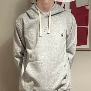 Ljusgrå hoodie från Polo Ralph Lauren - Säljer en stilren ljusgrå hoodie från Polo Ralph Lauren med klassisk logga broderad på bröstet. Tröjan har huva med dragsko och en stor magficka. Perfekt för en avslappnad och snygg look. Helt ny och inga defekter om ni har frågor eller funderingar är det bara att höra av er! 