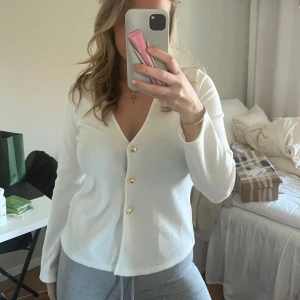 Vit kofta med guldknappar - Säljer en stilren vit kofta med snygga guldknappar och krage. Tröjan har lång ärm och är i ett mjukt material som passar perfekt till många outfits. Enkel och klassisk design.